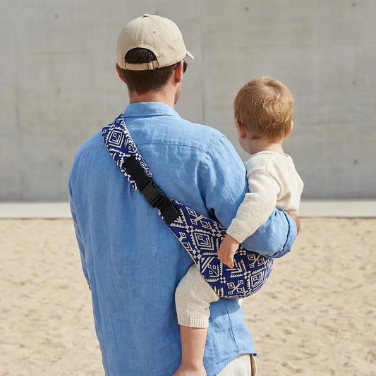 Needella CozyCarry Hüfttrage im Aztek-Stil in Blau-Weiß, Mutter trägt ihr Baby nah am Körper im Alltag