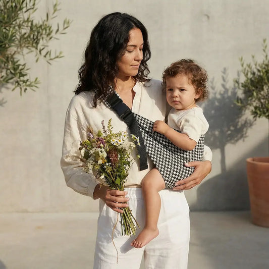 Needella CozyCarry Hüfttrage im Hahnentrittmuster in Schwarz-Weiß, Mutter trägt ihr Baby nah am Körper im Alltag