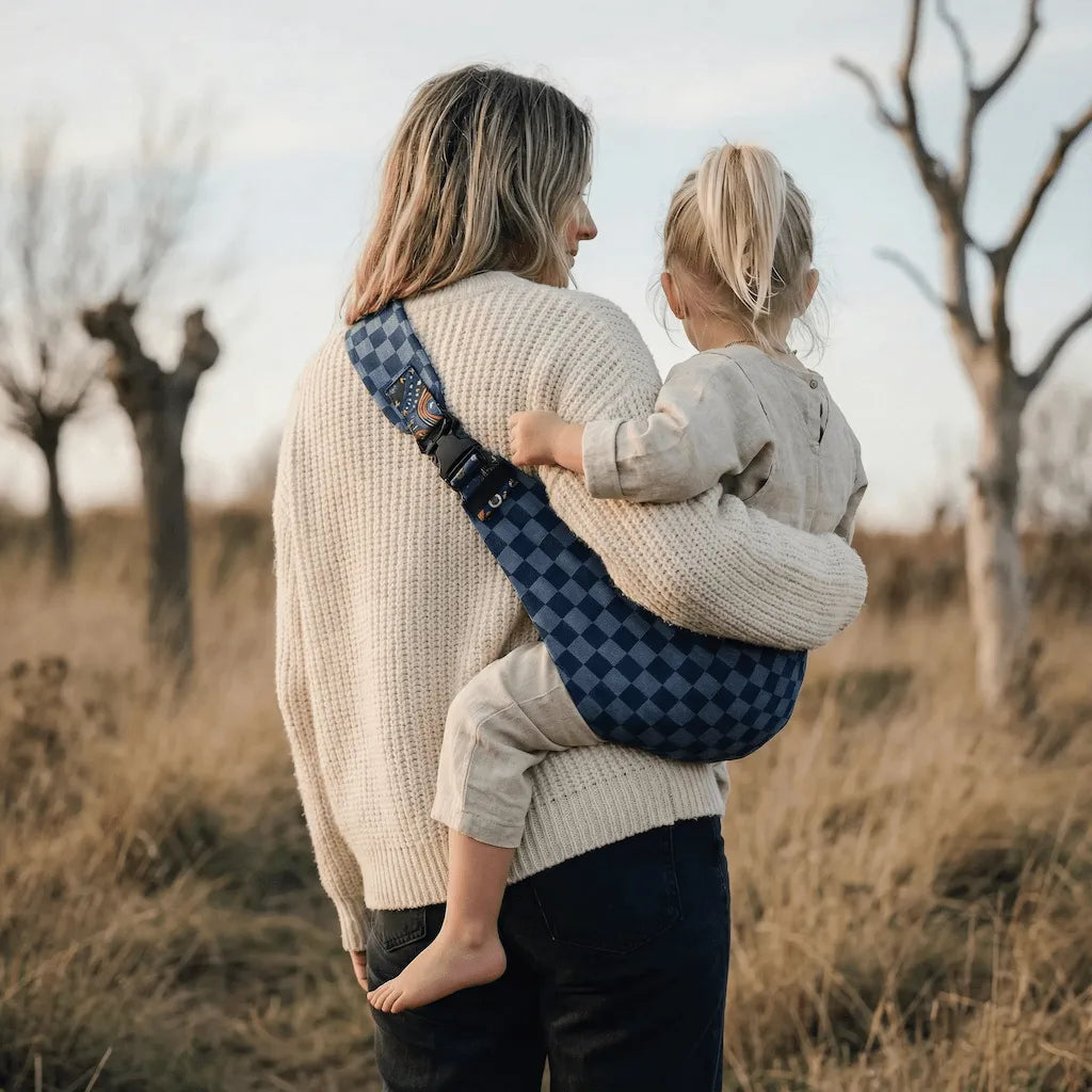 Needella CozyCarry Hüfttrage in Blau kariert, Eltern tragen ihr Baby entspannt im Alltag