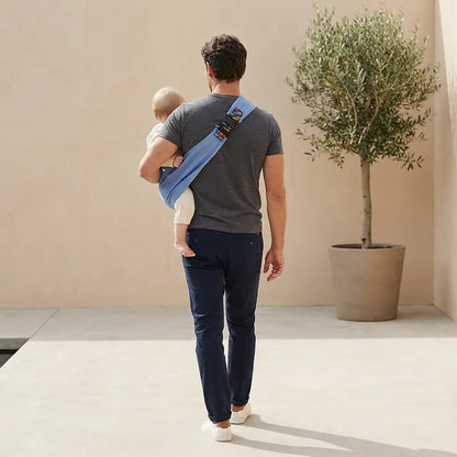 Needella CozyCarry Hüfttrage in Hellblau, Mutter trägt ihr Baby nah am Körper im Alltag