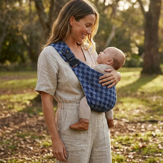 Needella CozyCarry Hüfttrage in Blau kariert, Mutter trägt ihr Baby nah am Körper im Alltag
