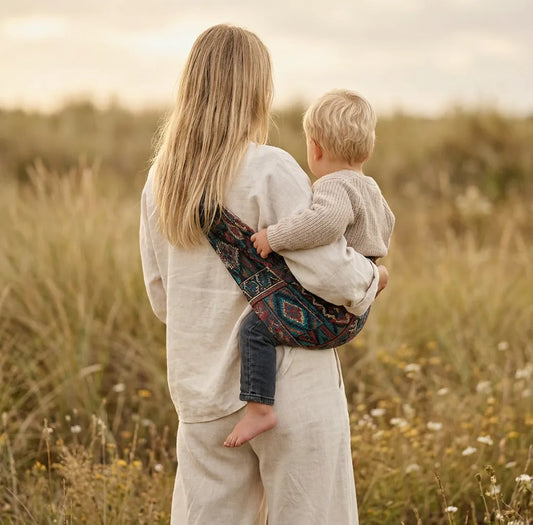 Needella CozyCarry Hüfttrage in Vintage, Mutter trägt ihr Baby nah am Körper im Alltag