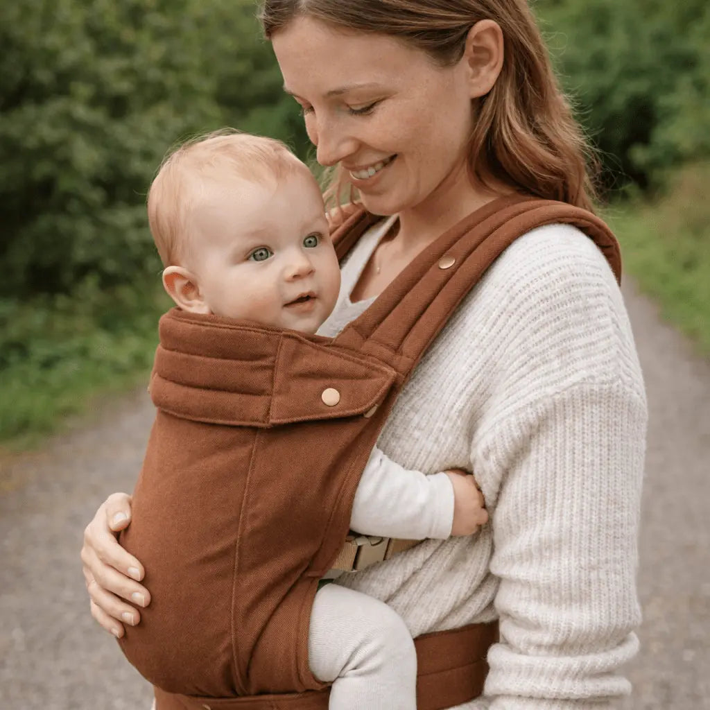 Needella Embrace Babytrage in Braun, Mutter trägt ihr Baby nah am Körper im Alltag