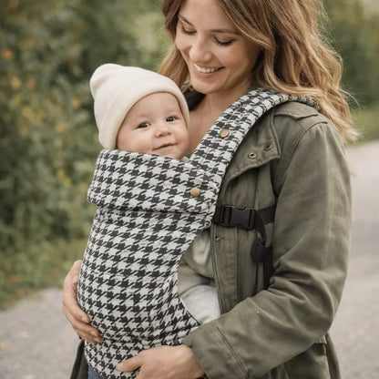 Needella Embrace Babytrage im Hahnentrittmuster in Schwarz-Weiß, Mutter trägt ihr Baby nah am Körper im Alltag