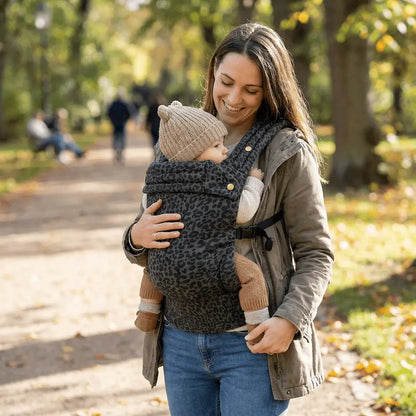 Needella Embrace Babytrage im Leopardmuster in Grau, Mutter trägt ihr Baby nah am Körper im Alltag