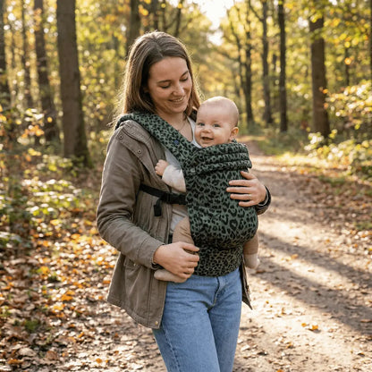 Needella Embrace Babytrage im Leopardmuster in Grün, Mutter trägt ihr Baby nah am Körper im Alltag