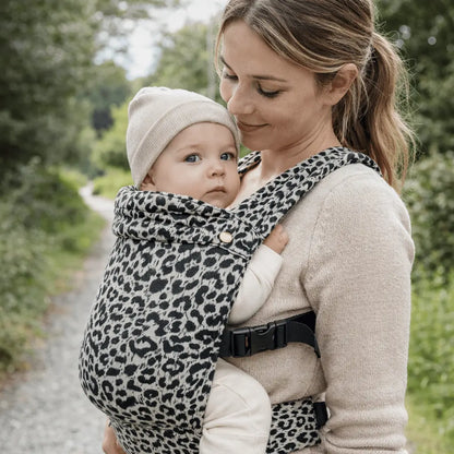 Needella Embrace Babytrage im Leopardmuster in Weiß, Mutter trägt ihr Baby nah am Körper im Alltag